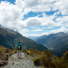 A man hiking on the Key Summit with views of the valleys under the white fluffy clouds, Routeburn Track, South Island. Vertical format
