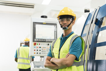 Young Asian male worker in yellow helmet smile with confidence in front of machine in factory production line with copy space.
