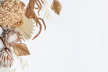 Rustic dried flower arrangement of King Proteas, Hydrangea, Ruscus leaves, Amaranthus and Palm fronds, photographed from above, on a white background. Earthy tones of brown, cream, pink and gold.