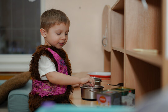 cute caucasian boy in carnival costume of bear playing with toy kitchen in kindergarden pretending cooking on stove. Image with selective focus