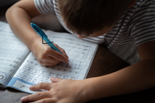 close up top view of boy's  hands writing russian cursive letters in a copybook. Image with selective focus