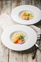 Two servings of seafood risotto in white plates. Egg with smoked mackerel pate. Honey orange tomato. Gourmet cuisine. Food photography and styling. Mediterranean Kitchen Vertical shot. Copy space