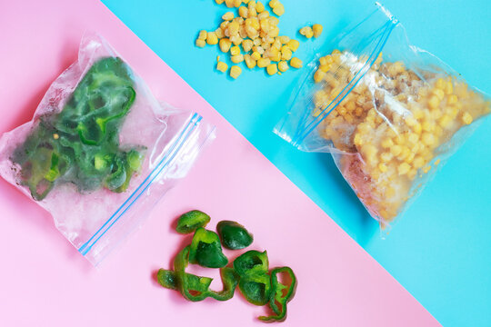 Packets of frozen scattered vegetables on blue and pink background close-up.