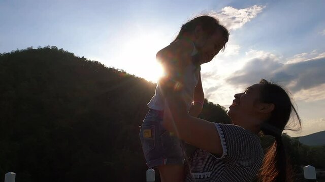 Happy mother holding little girl smiling and playing on sunset background in the park.