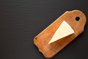 Pecorino Romano Cheese on a rustic wooden board on a black background, top view. Flat lay, overhead, from above. Copy space.