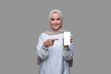 Beautiful woman in hijab is holding a mobile phone and pointing to the phone screen with a smile.