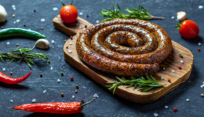 Grilled sausages on a dark wooden board with rosemary, salt and peper
