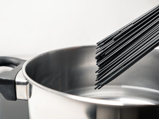 Uncooked black spaghetti above saucepan