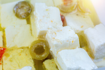Feta cheese cubes with spices and olives in oil marinade. Close up, macro photo.