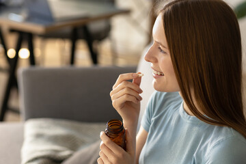 Smiling young woman puts food supplement capsule or vitamins in her mouth. Copy space - obrazy, fototapety, plakaty