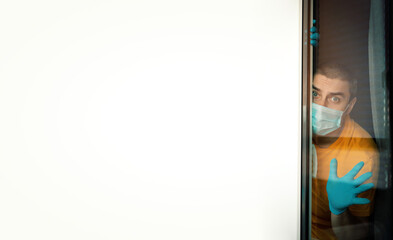  Quarantine man in medical mask on face  looking through the window.
