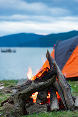 Camp fire in the mountains. Tent on the lake shore. Burning fire