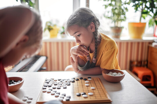 Brother and sister playing Chinese chess go at home, sibling have fun together with igo go stones, without gadgets, traditional Chinese board game, digital detox, happy family moments
