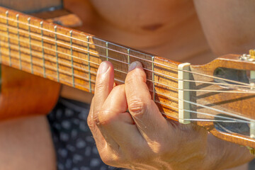 A man sits in the courtyard of a village house and plays an acoustic guitar. Close-up. Soft focus