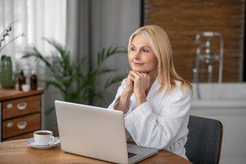 Pretty blonde woman sitting at the laptop and looking thoughtful