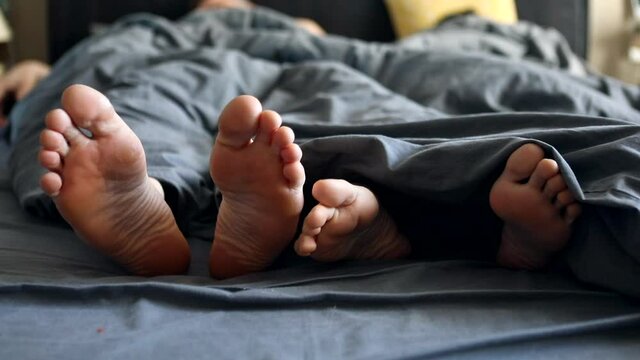 couple legs woman and man under the grey blanket in bed