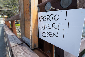 White sign hanging indicating that a restaurant is finally open after quarantine period due to coronavirus. "Aperto", "Ouvert", "Open" mean "Open".