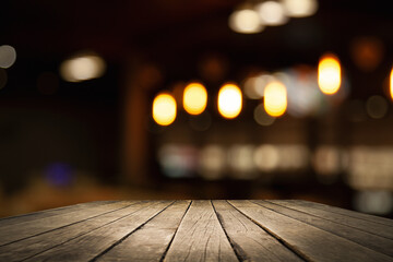 empty wooden table on blurred light gold bokeh of cafe-restaurant window on dark background, place for your products, blurred cafe interior.