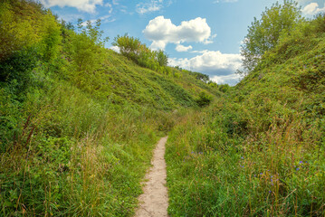 Fototapeta na wymiar Summer landscape, road to clouds, path between hills overgrown with fresh grass and white clouds and blue sky in front