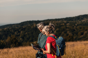 Active senior couple hiking in nature with backpacks, enjoying their adventure at sunset.