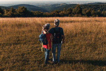 Naklejka na ściany i meble Active senior couple hiking in nature with backpacks, enjoying their adventure at sunset.