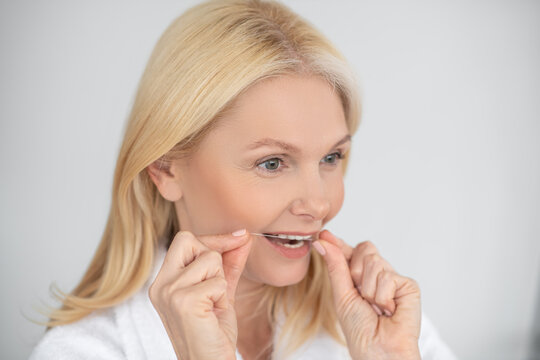A portrait picture of a woman brushing her teeth with a dental floss