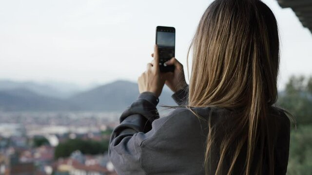 Woman take a photo, blurred city hills panorama on background