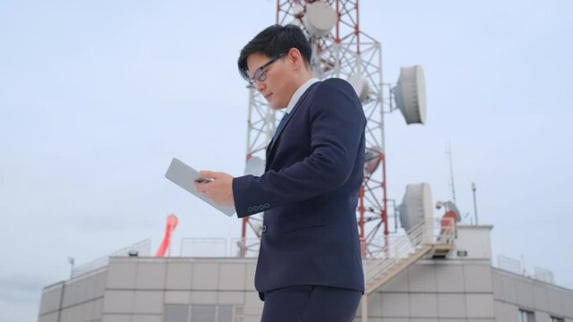 Business man use tablet and walk pass communication pole on rooftop of high building in big city. Concept of good support communication system help betty result in business management.