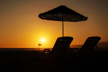 Beautiful sunset beach scene with chairs on sandy beach against yellow sky.