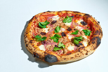 Delicious Italian wood-fired pizza with tomato sauce, mozzarella, olives and tuna on a gray background. Hard light.