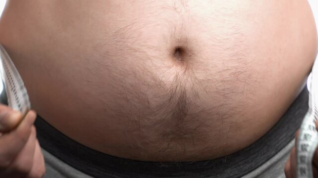 fat man measures the size of the abdomen with a centimeter measuring tape. the person suffers from excess weight.