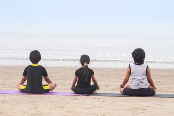 Gordijnen Back of boys and girl meditating in lotus position on mat practicing yoga at beach © Dishant