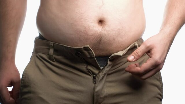 The man unbuttoning his pants and begins to touch his fat belly.Diet,obesity.Crumples hands and shakes his naked fat stomach.