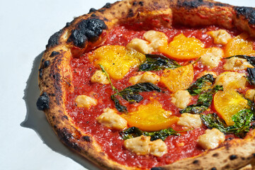 Delicious italian wood fired pizza with tomato sauce, yellow tomatoes and vegan cheese on a gray background. Hard light.