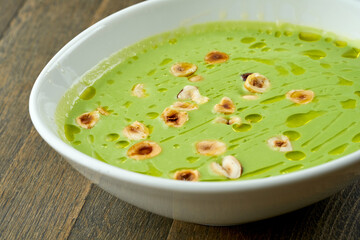 Diet food - green cream broccoli soup with hazelnuts and truffle oil in a white bowl on a wooden...