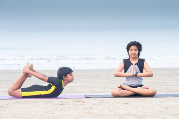 Two boys meditating and practicing yoga bow pose on exercise mat at beach