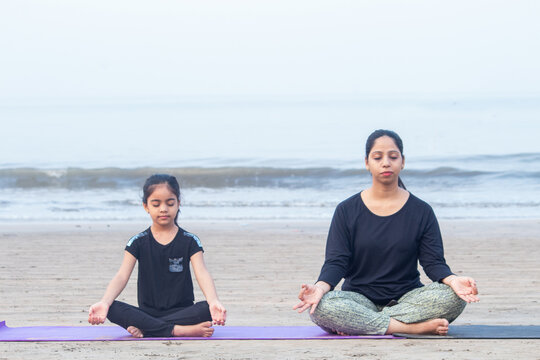 Mother and little daughter meditating on exercise mat at beach - Powered by Adobe