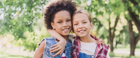 Two little girls hugging in the park. Diverse multi ethnic kids friends playing together outdoor. Summer fun, friendship, diversity, vacations concept