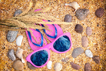 Beach scene. Sun straw hat, a pair of flip flop sandals, and sunglasses lying on sea coquina shells...