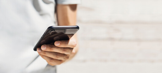 Using smartphone in a city. Panoramic banner. Male hand holding phone, man looking at mobile phone. Modern lifestyle, connection, communication, business, apps, technology concept