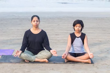Foto op Plexiglas Female yoga instructor with boy meditating in yoga lotus pose at beach © Dishant