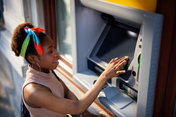 Beautiful african womn using ATM machine. Attractive young woman withdrawing money from credit card...