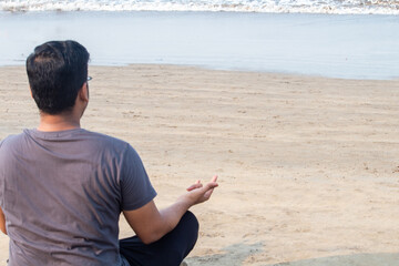 Rear view of man meditating in yoga lotus position at beach