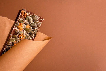 Top view on natural organic chocolate bar with nuts and seeds on brown paper background with copy space. Flat lay composition for sugar-free chocolate brand. Selective focus
