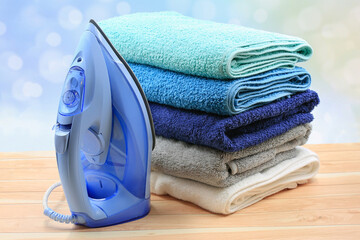 Stack of colorful towels with electric iron on wooden table over bokeh background.