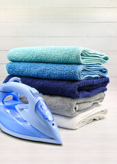 Stack of colorful towels with electric iron on white wooden table. Portrait view.