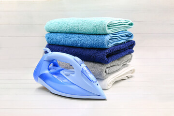 Stack of colorful towels with electric iron on white wooden table.