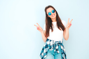 Young beautiful smiling female in trendy summer hipster clothes. Sexy carefree woman posing near light blue wall in studio. Positive model having fun indoors. Cheerful and happy