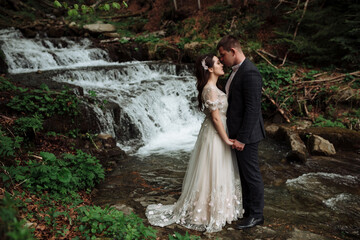 Fototapeta premium Wedding couple, bride and groom on the background of a waterfall in the woods