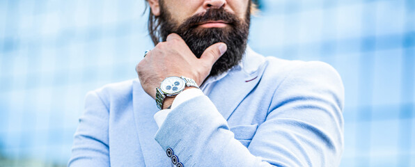 Man holds his watch. Portrait successful businessman in a business suit, using the watch on a city...